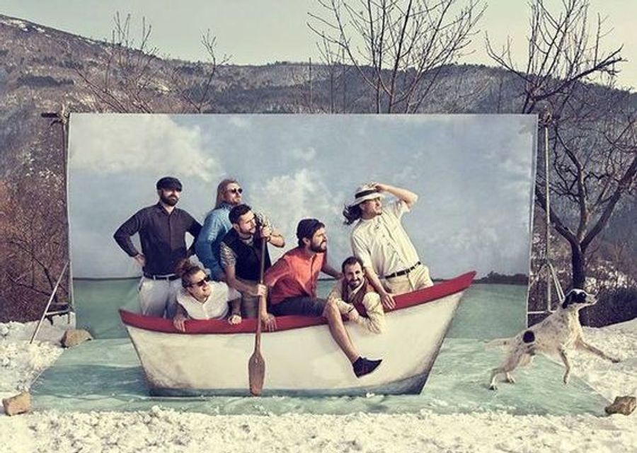 Groupe d'amis dans un Photo booth de mariage original avec du sable, une barque, des pagaies et une toile de fond imitant le ciel bleu